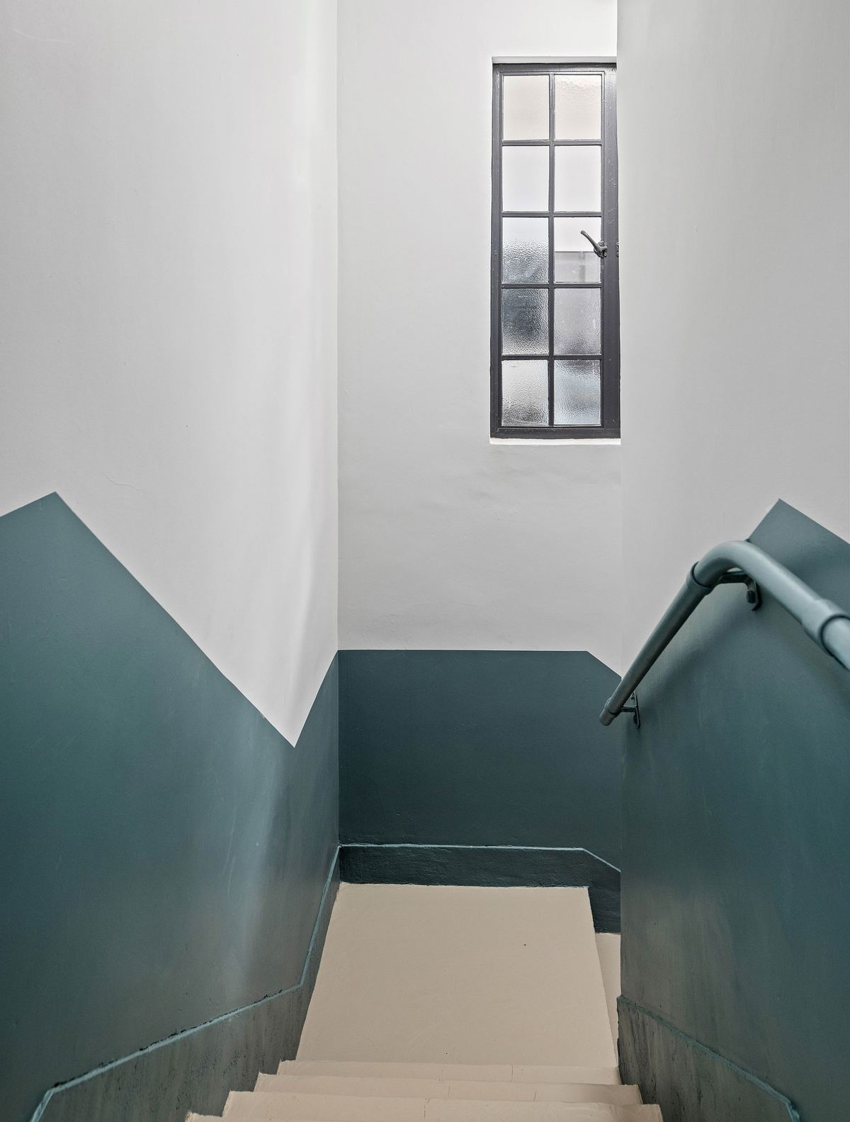 Stairwell in teal and white under a tall window