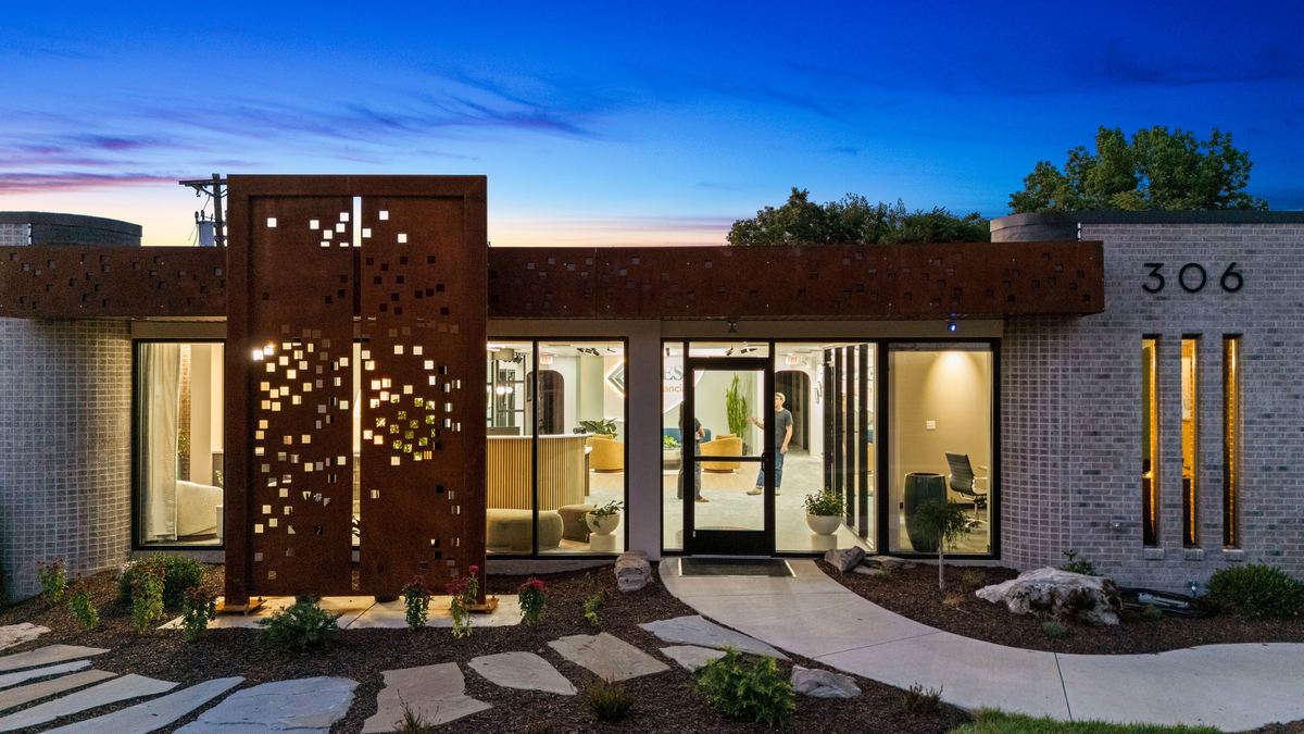 The perforated corten screen lit from inside at blue hour