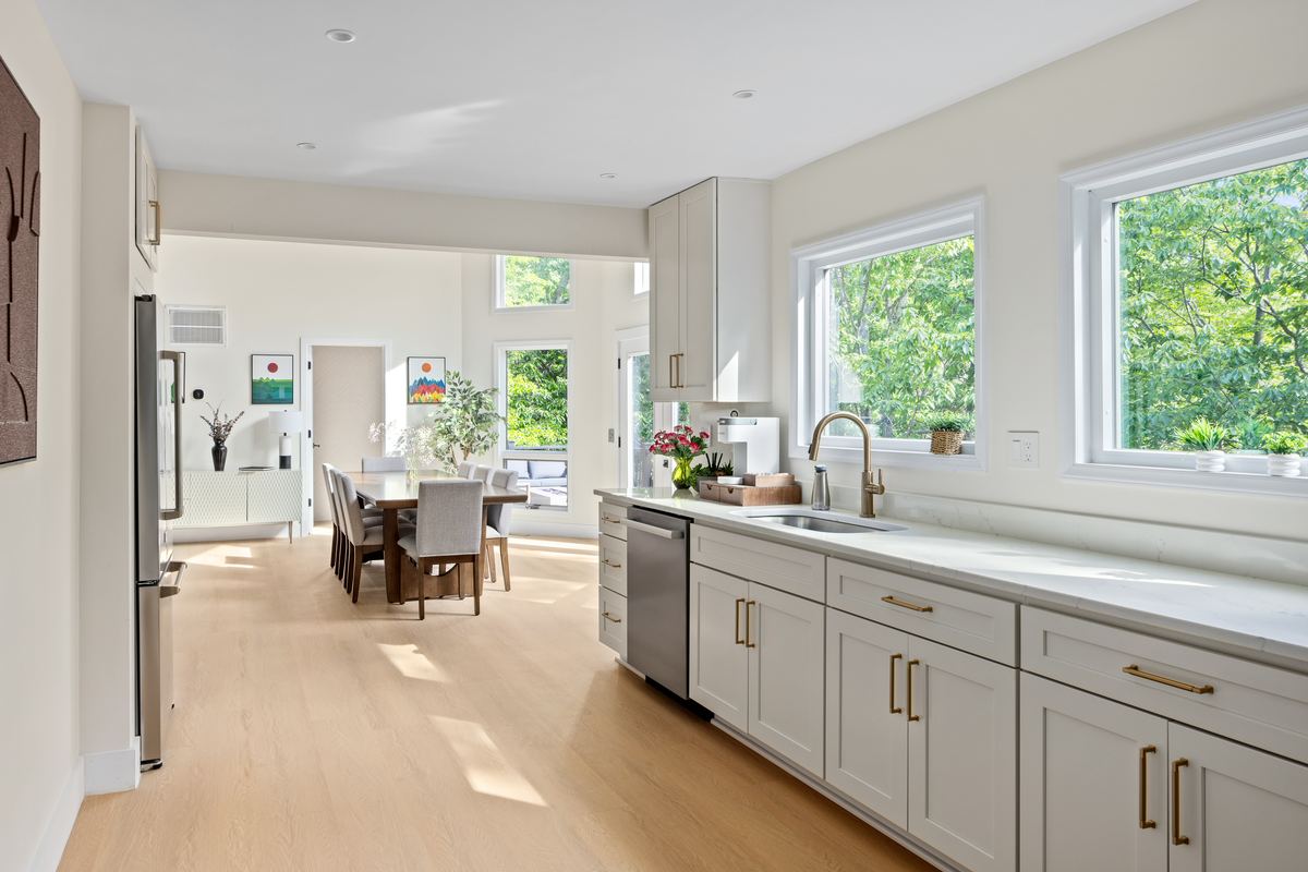 White kitchen with a long island and a wall of windows to the woods