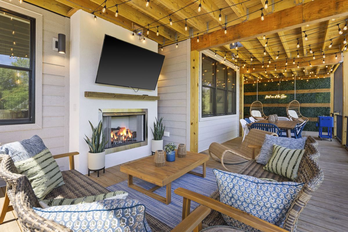 Covered porch with a fireplace, rattan seating and string lights over the river